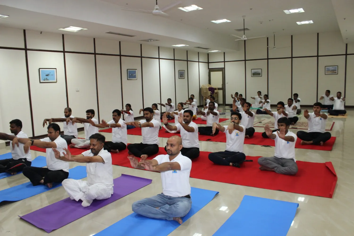 A large group seated on mats with arms stretched forward during a session