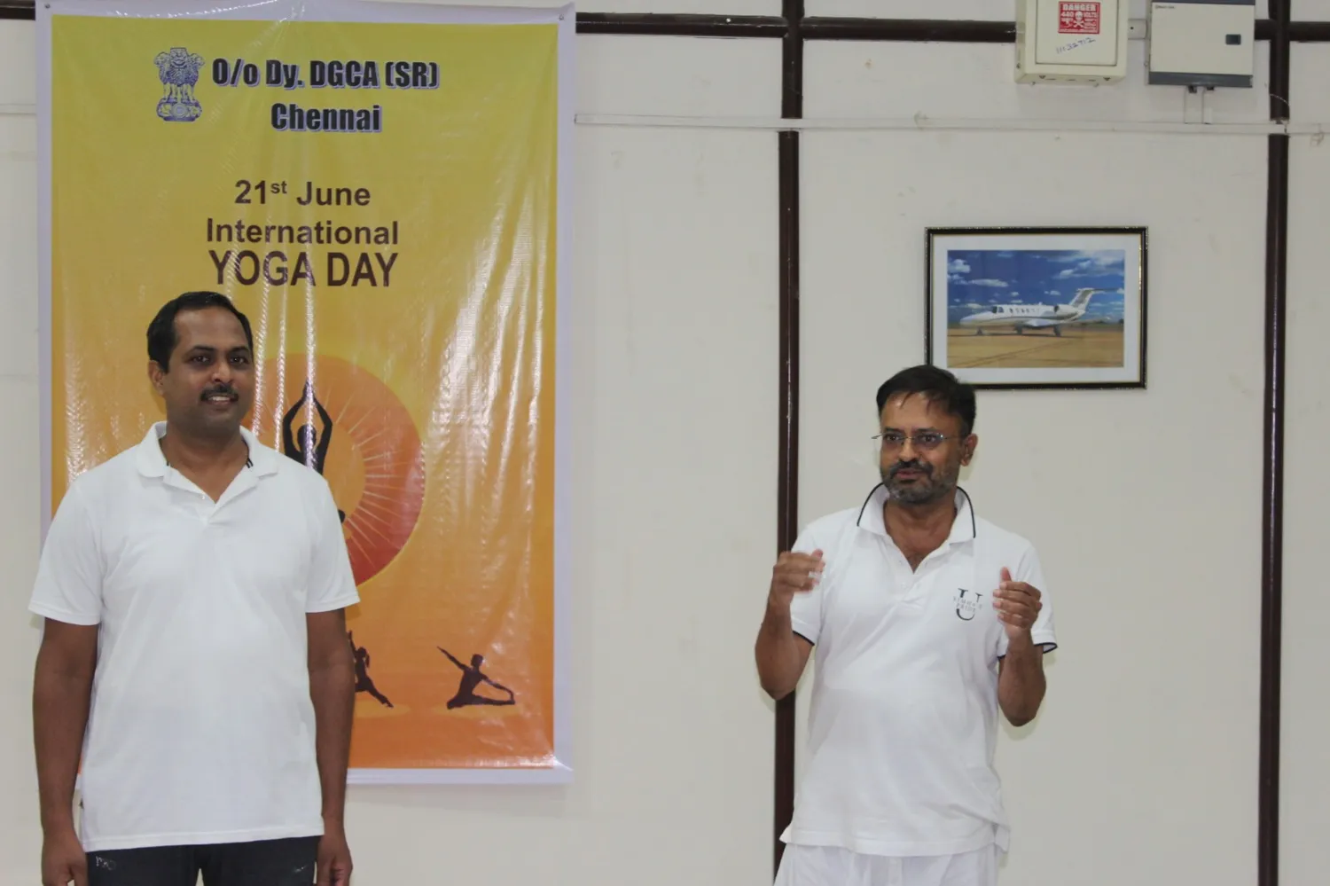 Two instructors addressing the class beside an International Yoga Day banner