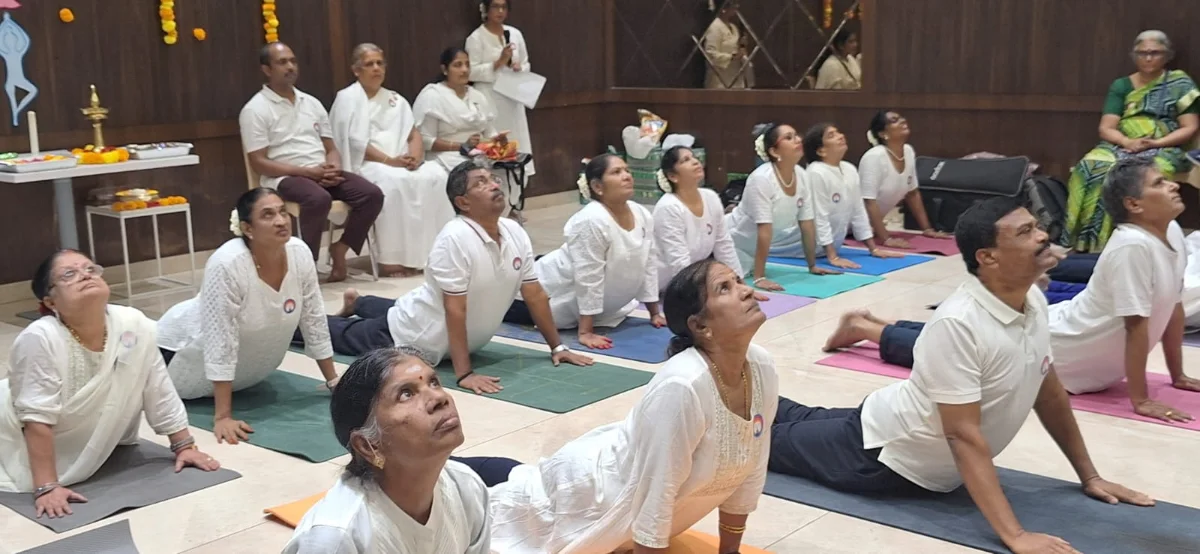 A hall of students in white practising upward-facing dog on coloured mats